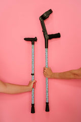 Two crutches held by hands against a pink background