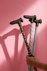 Three walking sticks with patterned handles held against a pink background