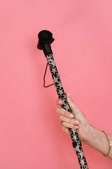 Hand holding a walking cane with a patterned handle against a pink background