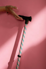Floral-patterned walking cane held by a hand against a pink background