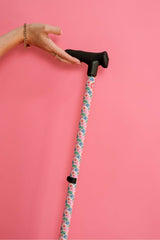 Cane with floral pattern handle held by a hand against a pink background