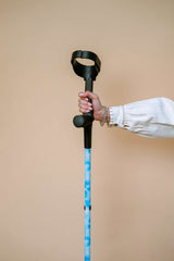 Hand holding a blue and black cane against a beige background