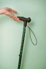 Hand holding a walking cane with a patterned handle against a light green background