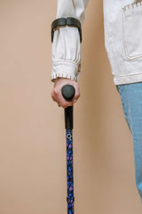 Person holding a walking cane with a patterned handle against a beige background