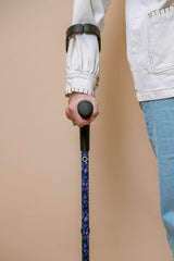 Person holding a purple butterfly walking crutch with a handle against a beige background