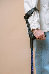 Person holding a purple butterfly print crutch against a beige background