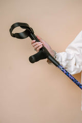 Person holding a purple butterfly print crutch at an angle against a beige background