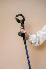 Person holding a black and purple walking cane against a beige background