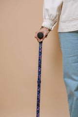 Person holding a walking cane with a patterned handle against a beige background