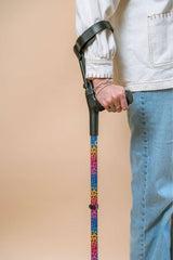 Person holding a colourful leopard print rainbow crutch against a beige background