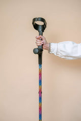 Cane with colourful leopard print design and black handle held by a person against a beige background