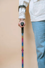 Person holding a colourful leopard print walking cane against a beige background