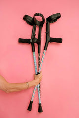 Person holding crutches with colorful grips against a pink background