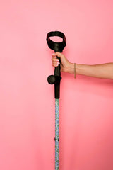 Hand holding a walking stick with a decorative handle against a pink background