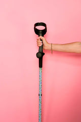 Hand holding a walking stick with a black handle against a pink background