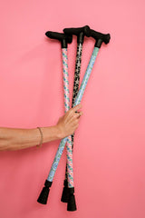 Three walking sticks with patterned grips held by a hand against a pink background