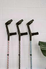 Three crutches with patterned grips against a white tiled wall.