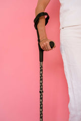 Person holding a cane with a patterned handle against a pink background