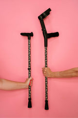 Two crutches held by hands against a pink background