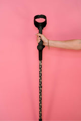 Hand holding a black cane with a patterned starfish funky bottom against a pink background
