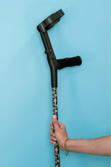 Hand holding a black and beige starfish print cane against a blue background