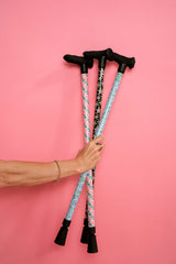 Three walking sticks with patterned handles held by a hand against a pink background