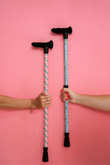 Two walking sticks held by hands against a pink background