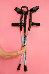 Three crutches with colourful handles held by a person against a pink background