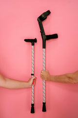 Two crutches with floral patterns held by hands against a pink background