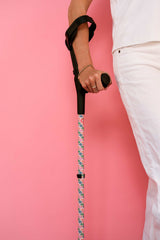 Person holding a floral-patterned cane against a pink background