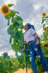 Lady stood in sunflowers using a pair of crutches designed with deep ocean blues and streaks of gold lightning