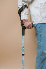 Person holding a walking crutch with a blue pattern against a beige background