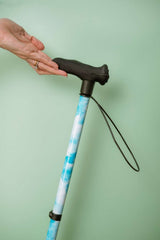 Cane with blue and white sky pattern held by a hand against a light green background