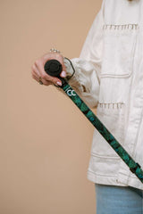 Person holding a camera with a green strap against a beige background