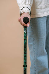 Person holding a green walking stick against a beige background