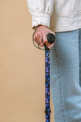 Person holding a walking stick with a decorative purple and blue handle against a beige background