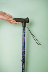 Hand holding a walking cane with a patterned handle against a light green background