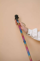 Hand holding a colorful rainbow leopard print walking stick against a beige background