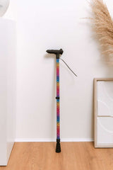 Colourful ergonomic walking cane on a wooden floor with a white wall and decorative elements in the background.