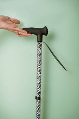 Hand holding a zebra-patterned walking stick against a light green background