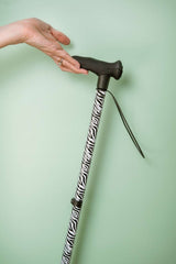 Cane with zebra pattern handle held by a hand against a light green background
