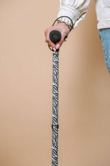 Person holding a zebra-patterned walking cane against a beige background