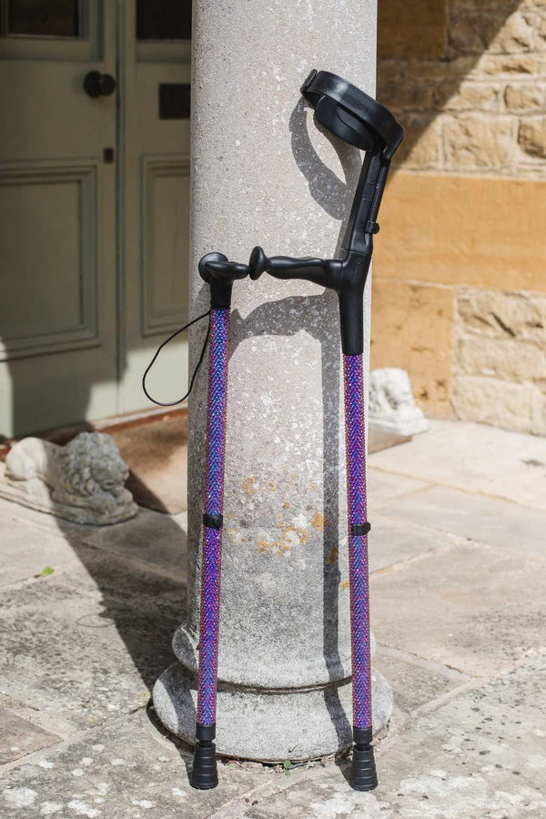 Purple walking stick and single crutch against a stone pillar and building exterior.
