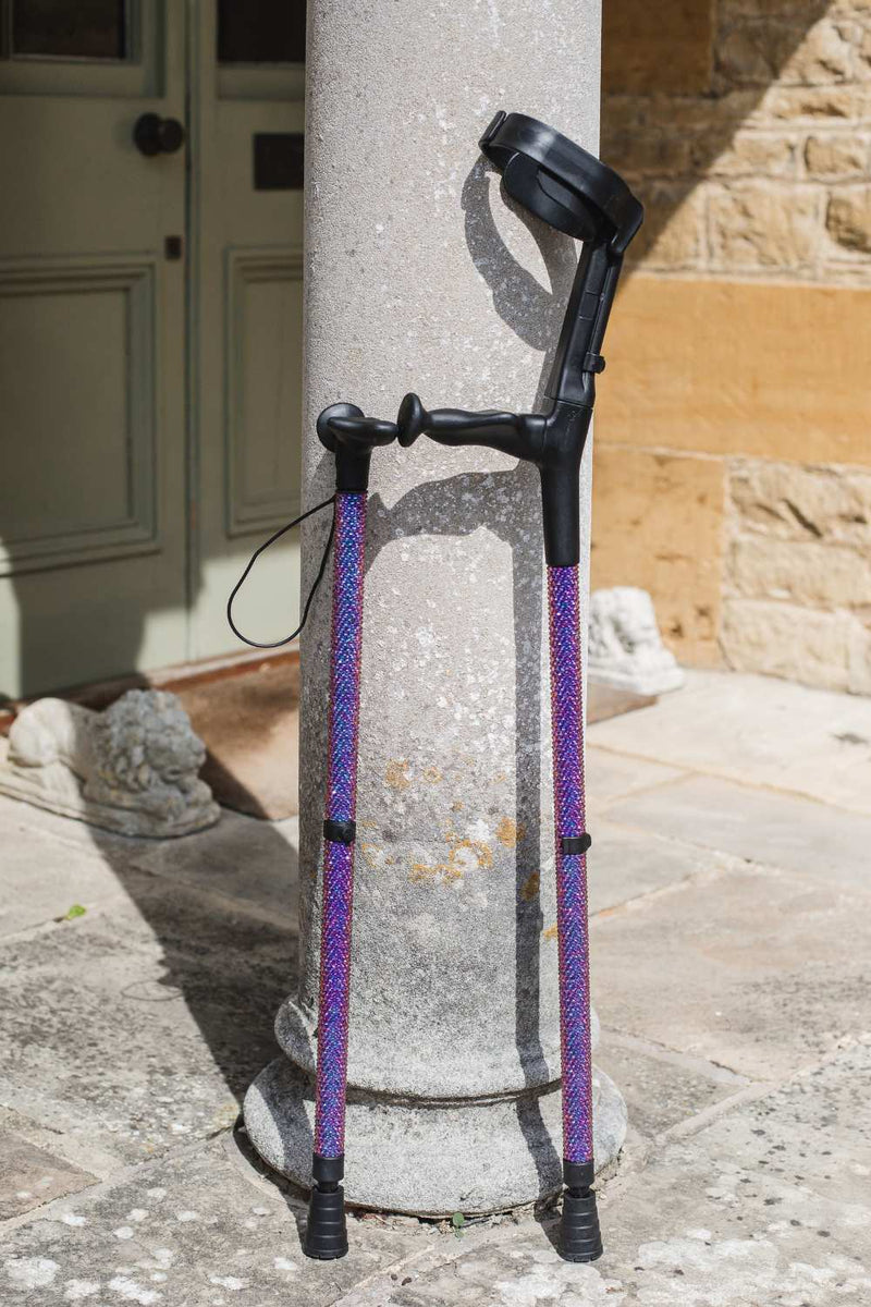 Purple walking stick and single crutch against a stone pillar and building exterior.