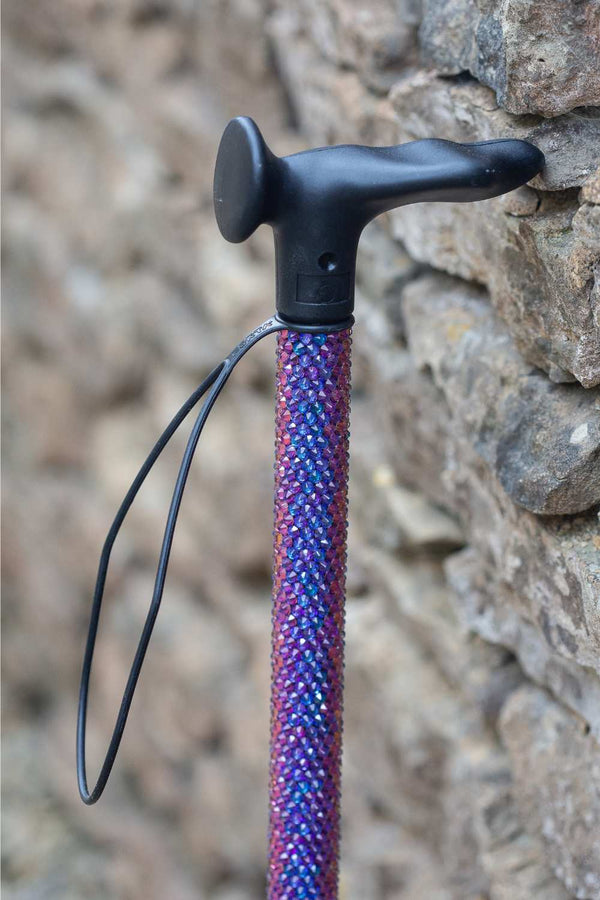 Purple textured walking stick with black handle against a stone wall background