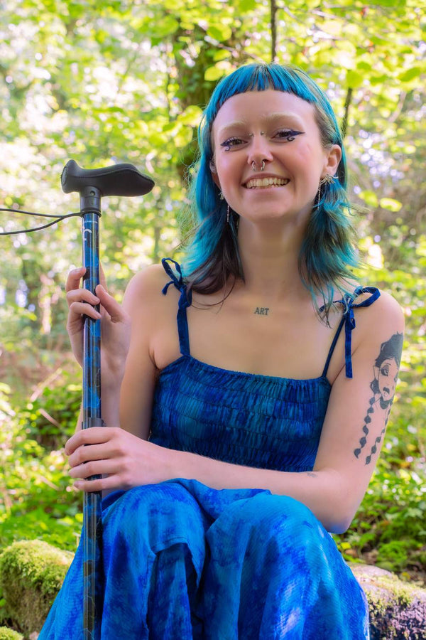 Person with blue hair holding a walking stick with a blend of deep ocean blues and electric gold lightning streaks 